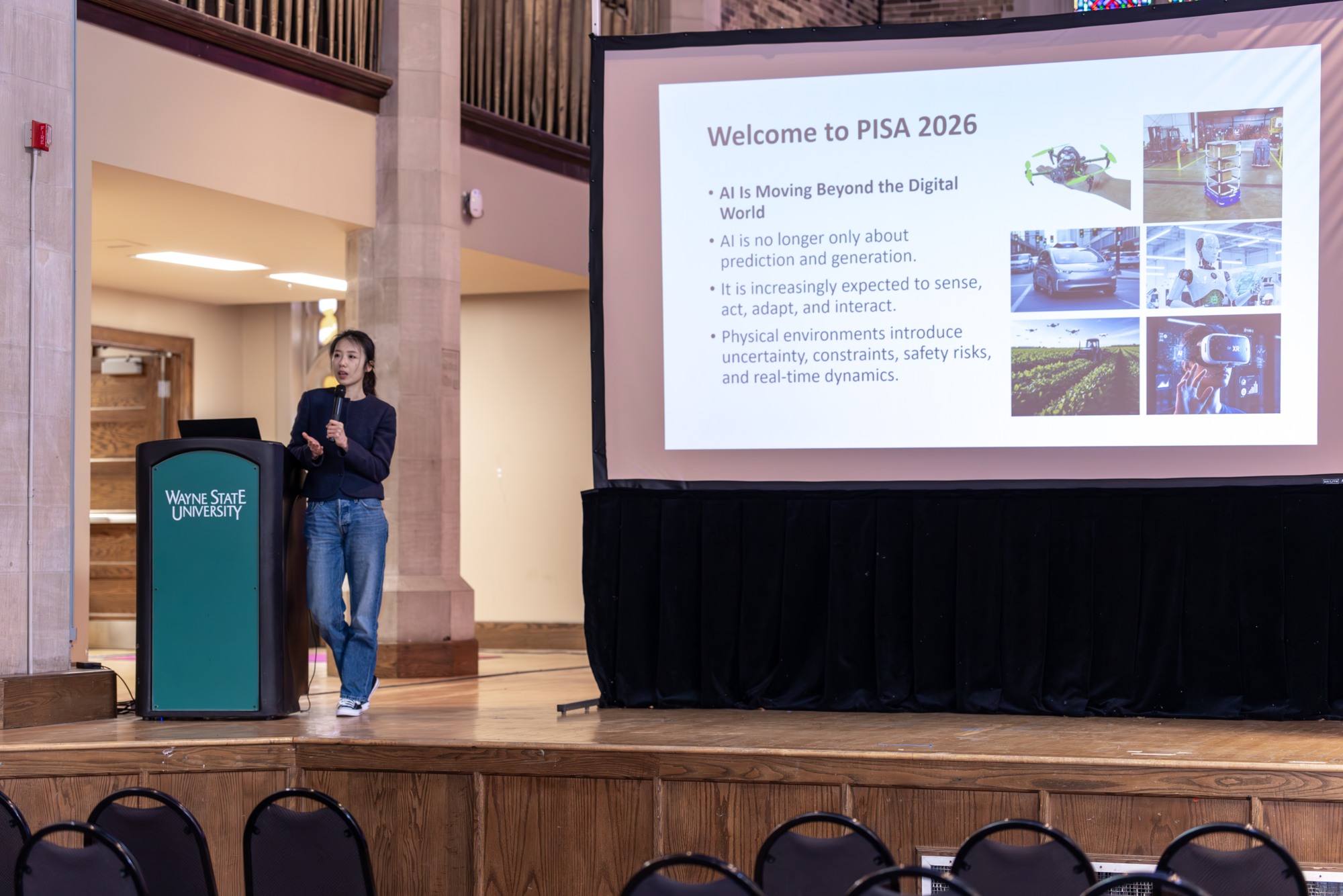 Chuchu Chen delivering the welcome remarks at IEEE PISA 2026, beside the Welcome to PISA 2026 slide at Wayne State University in Detroit.
