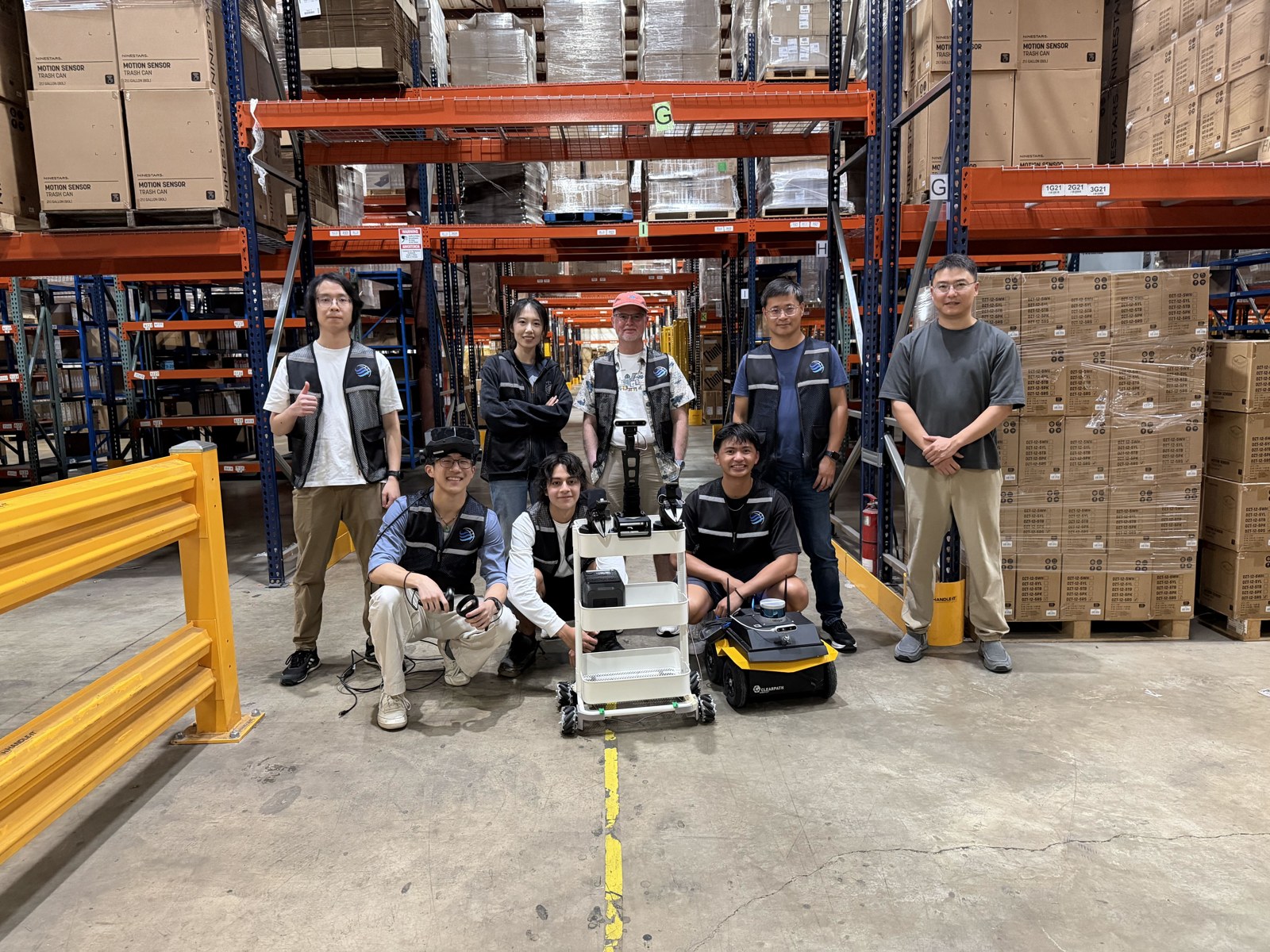 Chuchu Chen with students and collaborators alongside two research robots in EtailFlow's warehouse during Summer 2026.