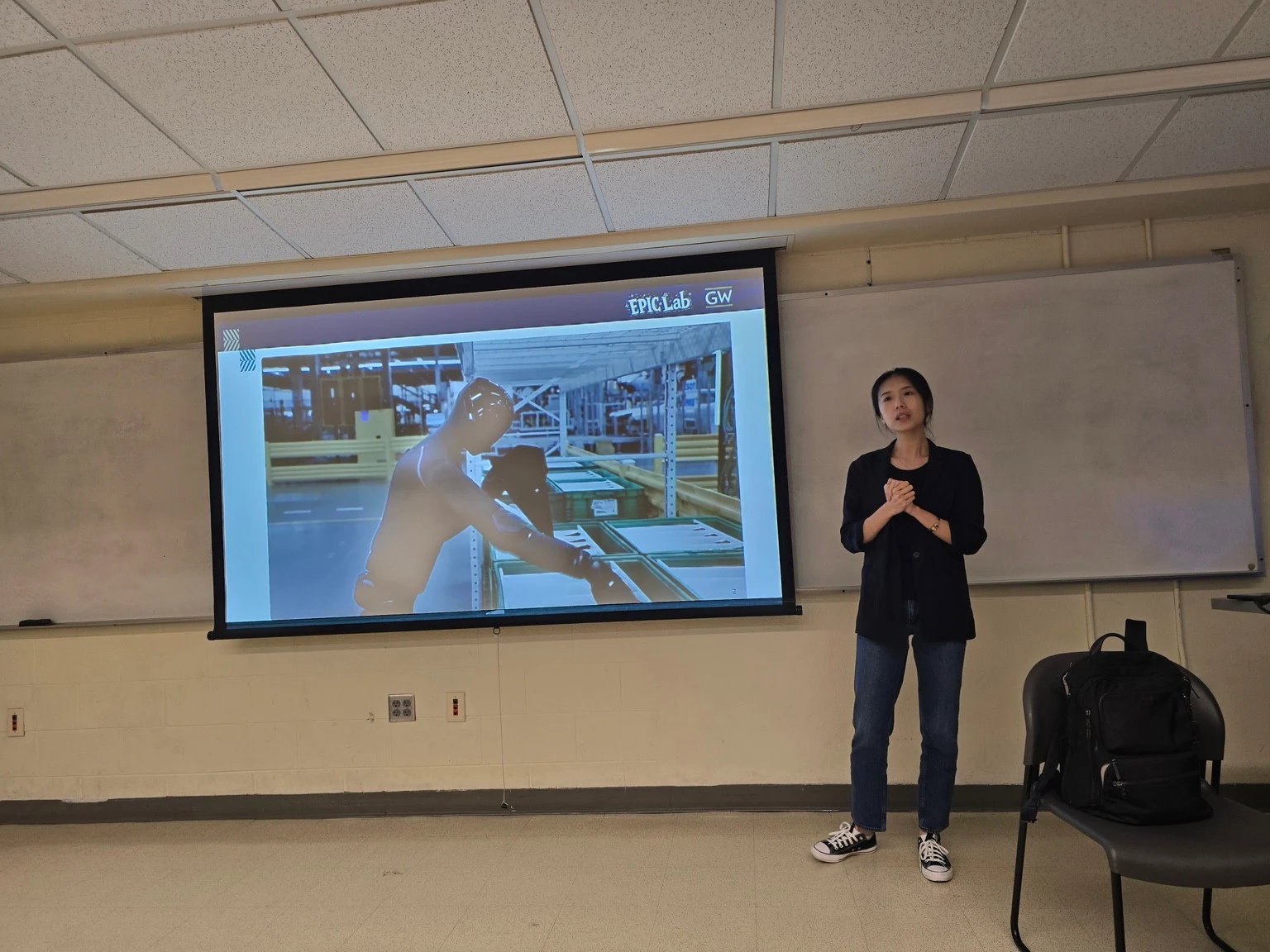 Chuchu Chen speaking beside a projected humanoid robot demonstration at the USF AI+X seminar on October 23, 2026.